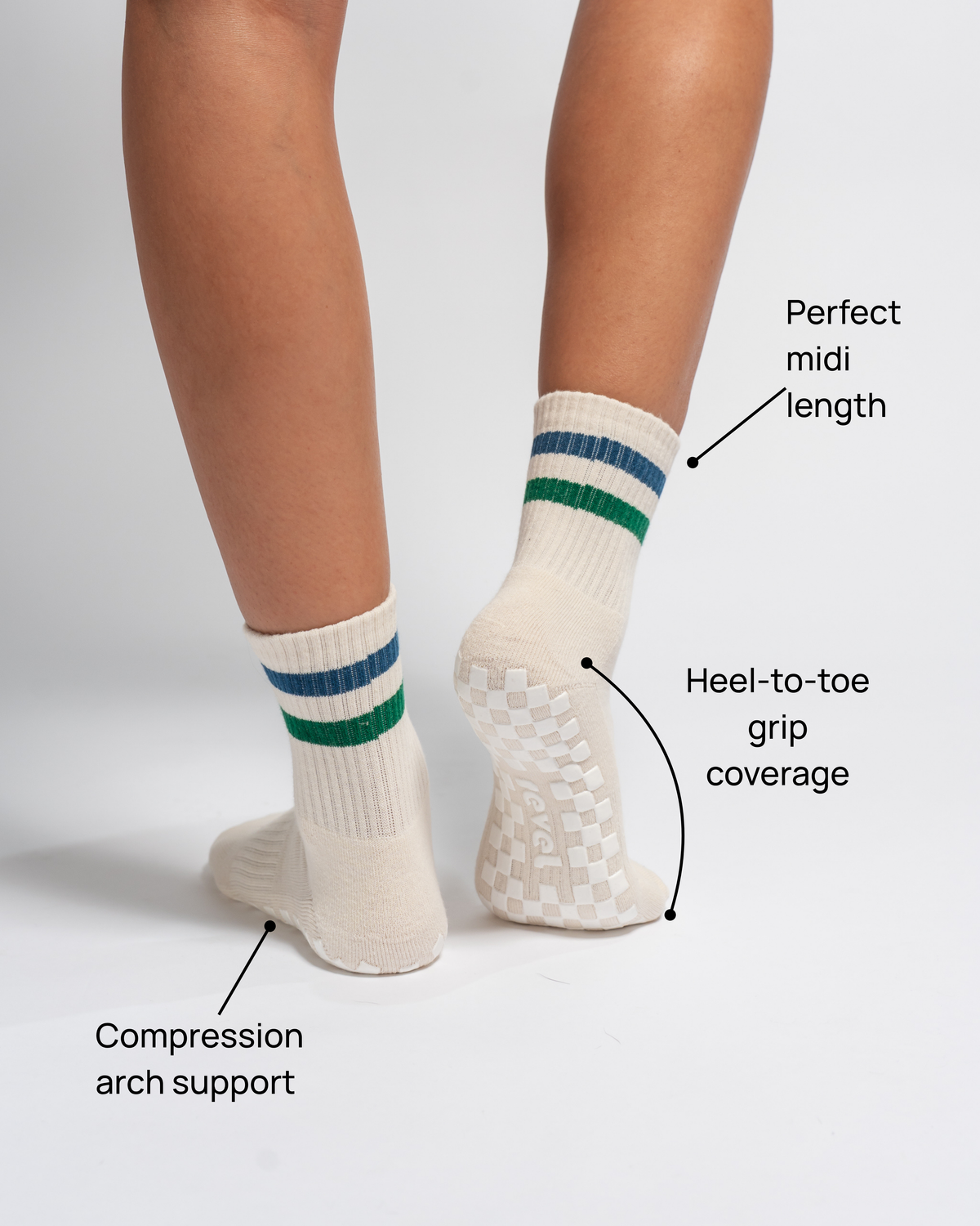 A person wears The Varsity Grip Sock by Revel in a cream color with green and blue stripes. Text highlights key features: compression arch support, heel-to-toe grip coverage, and a perfect midi length. Set against a plain white background, these ideal Pilates socks are designed by Revel for exceptional comfort and stability through every movement.