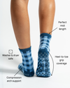 A person is seen from behind wearing The Prep Grip Sock by Revel Athletic in blue gingham. These midi-length socks are washer and dryer safe, offer compression arch support, and provide heel-to-toe grip coverage—making them perfect as barre or pilates grip socks for your next studio session.