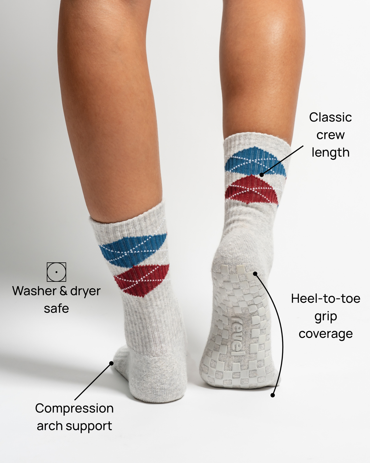 Two feet wearing The Legacy grip socks by Revel Athletic in light gray, featuring blue and red argyle patterns and classic crew length. Labels highlight features: washer & dryer safe, compression arch support, heel-to-toe grip coverage, and perfect for Pilates or everyday comfort.