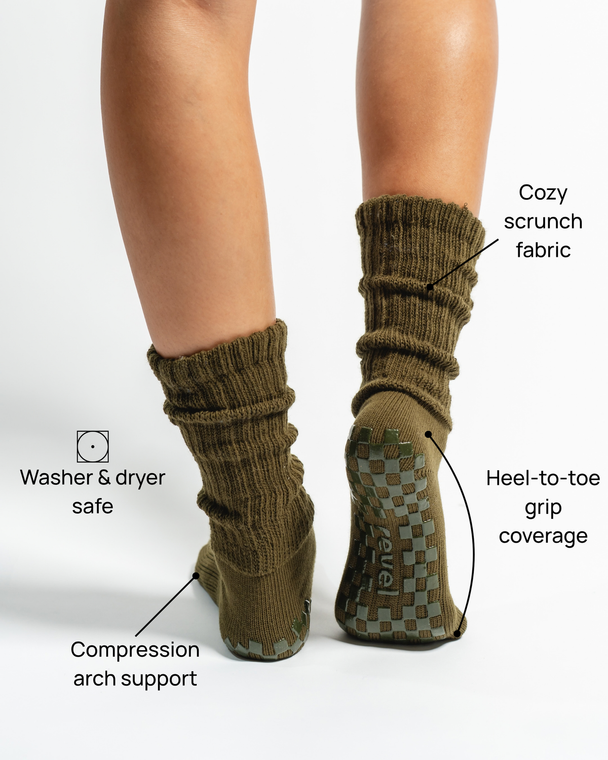 A person wearing Revel Athletic’s The Slouch - Olive grip socks stands on a white background; labels highlight cozy scrunch fabric, heel-to-toe grip, compression arch support, and washer/dryer safe features. Only legs and feet are visible. Ideal as non-slip yoga or Pilates socks for secure footing during your workout.
