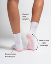A person wears The Pardon My French Grip Sock (Petal Pink) by Revel Athletic, featuring white fabric with petal pink grips on the bottom. Text highlights key features: Perfect midi length, Heel-to-toe grip coverage, and Compression arch support. The background is plain white.