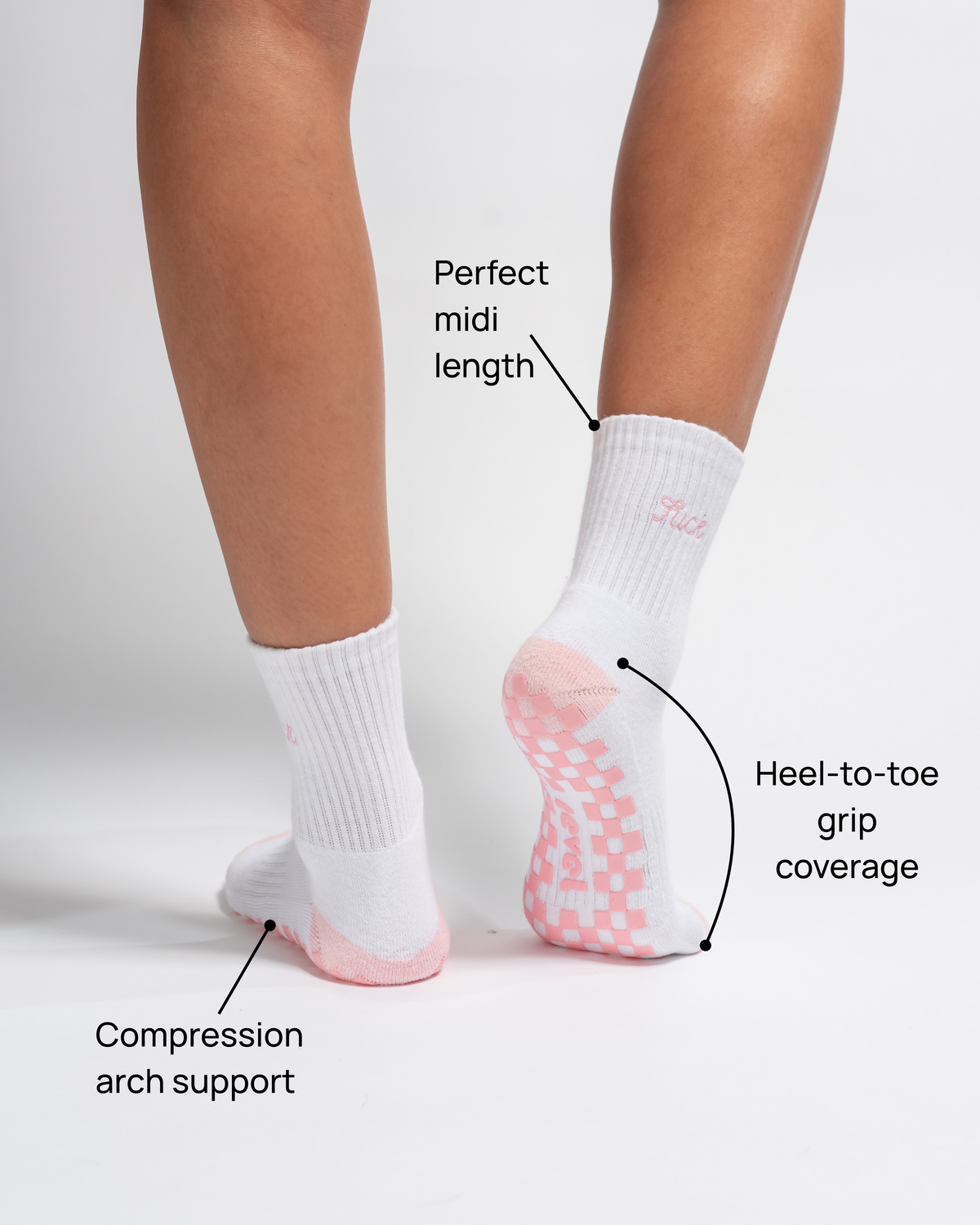 A person wears The Pardon My French Grip Sock (Petal Pink) by Revel Athletic, featuring white fabric with petal pink grips on the bottom. Text highlights key features: Perfect midi length, Heel-to-toe grip coverage, and Compression arch support. The background is plain white.