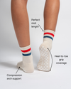 Two feet in Revel Athletic’s The Miss Americana Grip Sock in cream, featuring red and blue stripes. Text highlights the sock’s midi length, compression arch support, and full heel-to-toe grip coverage on the sole—making them ideal non-slip socks for enhanced stability. Set against a plain white background.