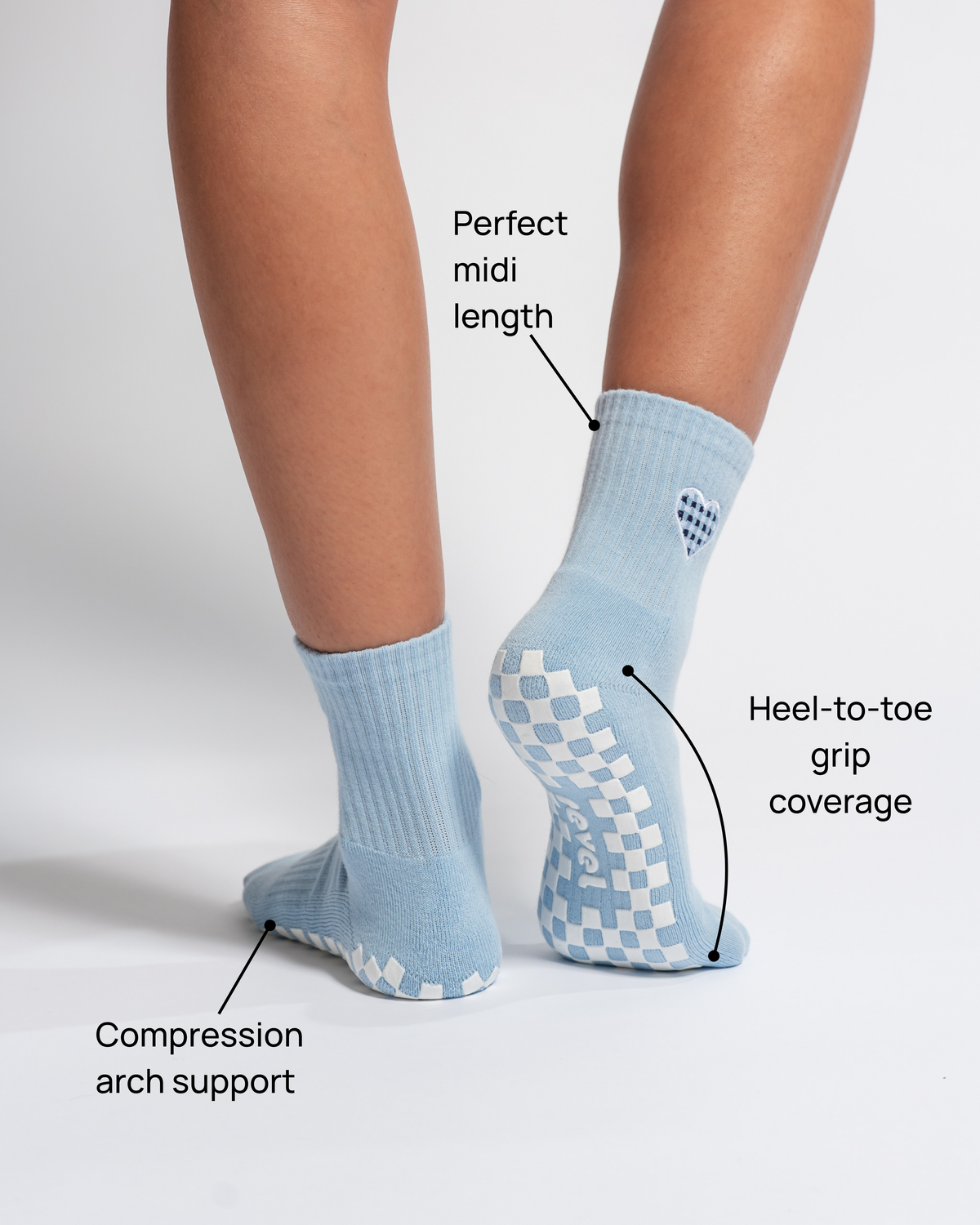Close-up of legs wearing Revel Athletic’s The Cross My Heart Grip Sock in light blue. Text highlights features: perfect midi length, heel-to-toe grip coverage, and compression arch support. Displayed against a white background.