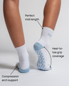 A person wears The Pardon My French Grip Sock (Baby Blue) by Revel Athletic—white socks with baby blue soles featuring a checkered grip pattern. Text labels highlight key features: perfect midi length, heel-to-toe grip coverage, and compression arch support. These yoga grip socks are designed for enhanced stability throughout every move.