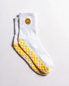 The I'm Fine Grip Sock by Revel Athletic is a pair of white socks featuring a yellow smiley face near the top and a yellow checkerboard pattern on the soles, designed for extra traction and perfect as Pilates socks; they're displayed on a white surface.