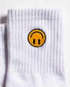 The I'm Fine Grip Sock by Revel Athletic features a white ribbed design with an embroidered yellow smiley face—sporting an upside-down mouth and outlined in black—on the upper part of the sock.
