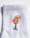 A detailed look at The Spritz Grip Sock by Revel Athletic—a white ribbed sock adorned with an embroidered Aperol Spritz in a tall glass, complete with ice cubes and an orange slice garnish—makes a playful addition to your Pilates grip socks collection.