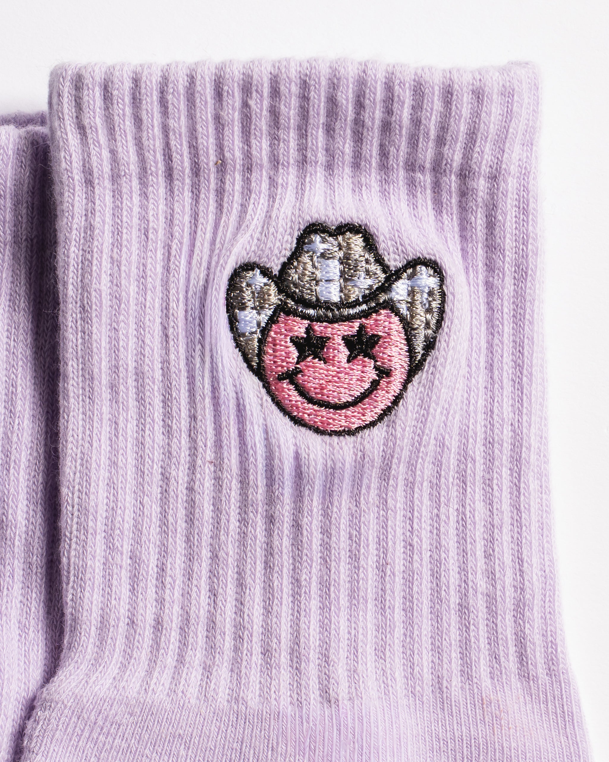 Lavender Austin grip socks with a cowboy-hat smiley face embroidery and a white non-slip traction sole
