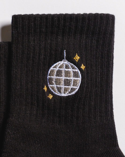 A close-up of The All Nighter Grip Sock by Revel Athletic—a black grip sock ideal for yoga or Pilates, adorned with an embroidered silver disco ball and four small yellow stars.