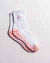 A pair of Revel Athletic’s The Pardon My French Grip Socks (Petal Pink) in white, featuring petal pink non-slip grips on the soles and toes, with “meh” embroidered near the top in pink. The socks are neatly stacked on a plain white background.