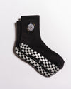 The All Nighter Grip Sock by Revel Athletic features a black design with a white checkerboard grip pattern on the soles and a small embroidered disco ball with stars at the ankle, making them perfect for yoga or Pilates. Shown here on a white background.