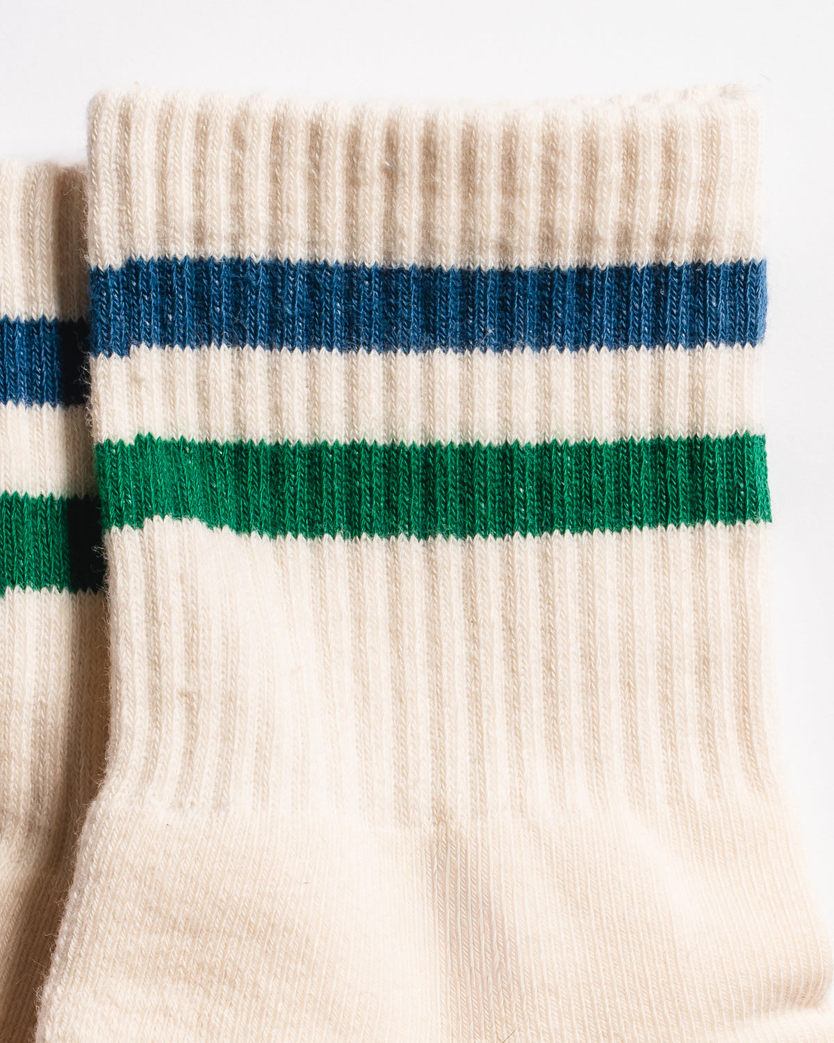Close-up of Revel’s The Varsity Grip Sock in cream, featuring blue and green horizontal stripes near the top and a ribbed texture, set against a white background.