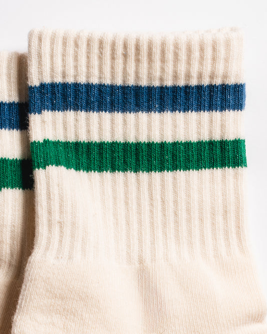 Close-up of Revel’s The Varsity Grip Sock in cream, featuring blue and green horizontal stripes near the top and a ribbed texture, set against a white background.