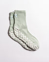A pair of Revel Athletic "The Tied & True Grip Sock" in light green, featuring ribbed cuffs, small blue bows near the top, and white non-slip grip patterns on the soles.