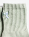 Close-up of The Tied & True Grip Socks by Revel Athletic in a light green ribbed design, featuring a small embroidered white and green bow near the top. The socks are positioned side by side on a white background.