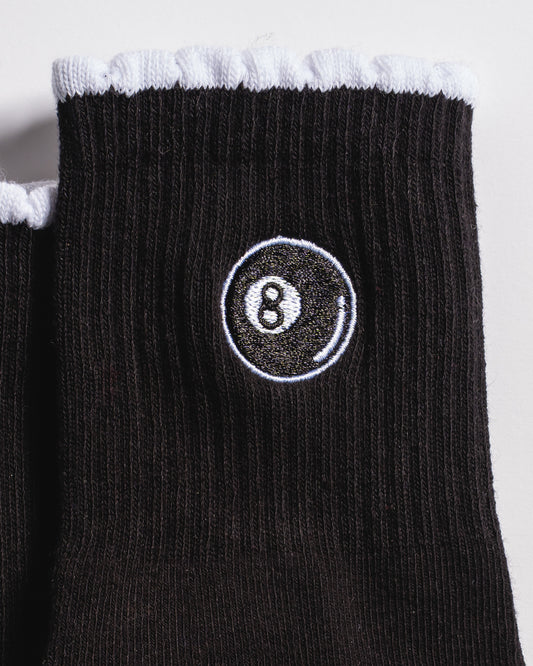 A close-up of the black ribbed fabric with white trim on Revel Athletic’s The Racked & Ready Grip Sock, featuring an embroidered 8-ball design inspired by billiards—perfect for barre or Pilates sessions.