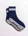 The Revel Athletic “The Country Club Grip Sock” features a blue crew design with two white stripes near the top and white checkered non-slip grips on the soles, displayed against a plain white background. Ideal as barre or Pilates socks, they provide added stability during your workout.