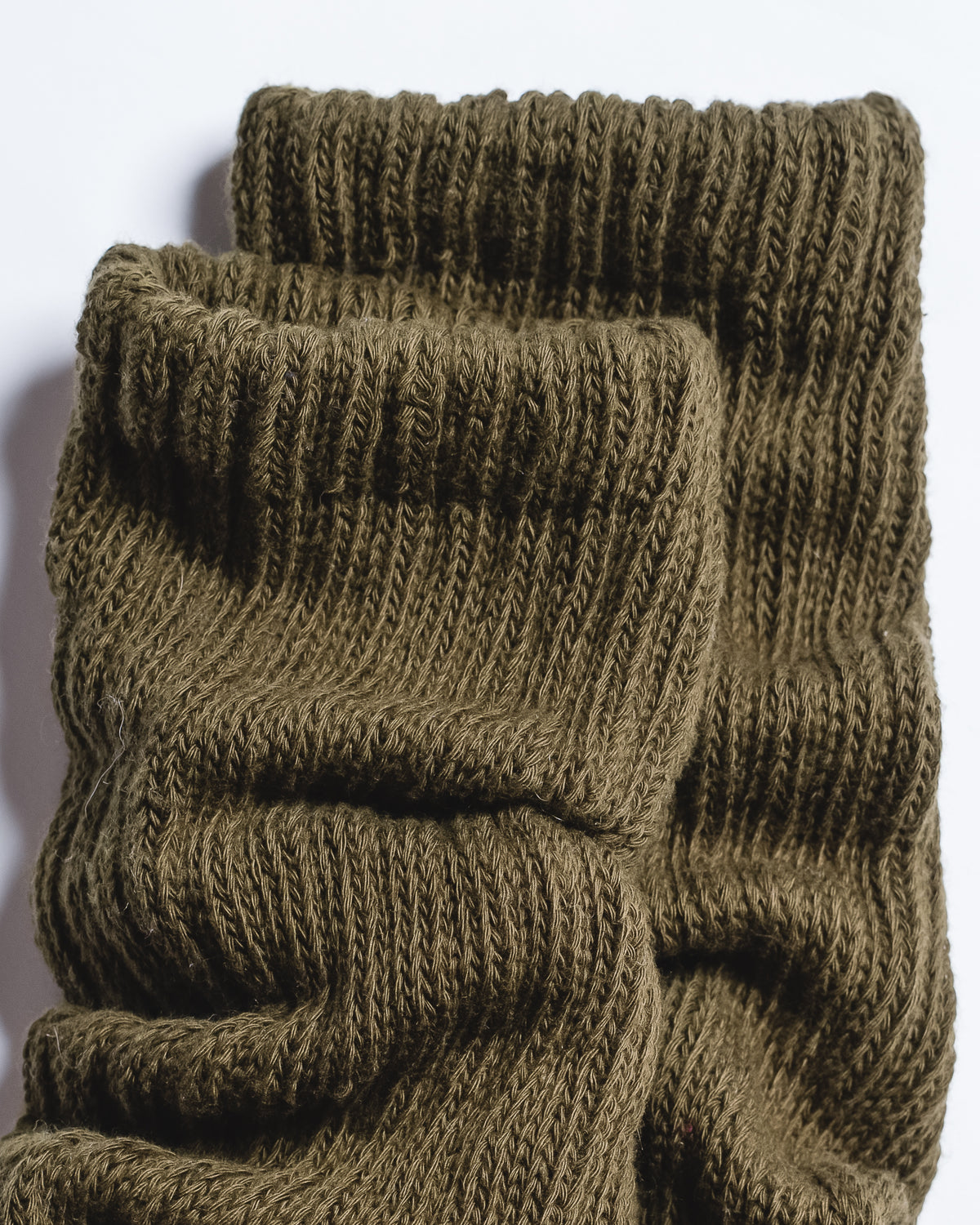 A close-up of two pairs of The Slouch - Olive grip socks by Revel Athletic, stacked together to showcase their olive green ribbed knit texture and folded cuffs against a white background.