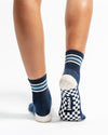 The MVP Pilates socks by Revel Athletic are navy blue with white stripes at the cuffs and checkered GripGrid soles featuring the word revel on the heel.