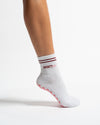 A white Revel Athletic Sportyish crew sock on a foot, featuring two maroon stripes at the cuff, the word SPORTYish in maroon text, and pink grip patterns on the sole.