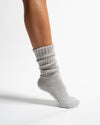 A person’s lower leg wearing Revel Athletic’s The Slouch - Grey Pilates grip sock, featuring a scrunched design and textured grips on the sole, set against a plain white background.