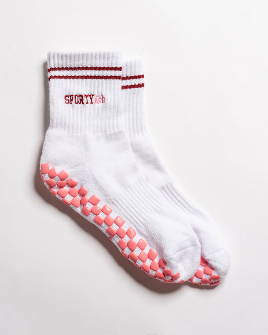 White The Sportyish crew socks by Revel Athletic featuring two maroon stripes at the cuff, the word SPORTYish embroidered in maroon, and pink grip pads on the soles.