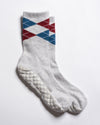 Revel Athletic’s The Legacy socks are white, crew length, featuring red and blue argyle patterns near the top and textured white GripGrid grips on the soles, perfect for Pilates, shown on a white background.