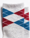 The Legacy socks by Revel Athletic are shown overlapping against a white background. These gray crew-length socks feature a red, blue, and white argyle pattern with diamond shapes and dotted lines and are designed with GripGrid technology for enhanced stability during Pilates or everyday wear.