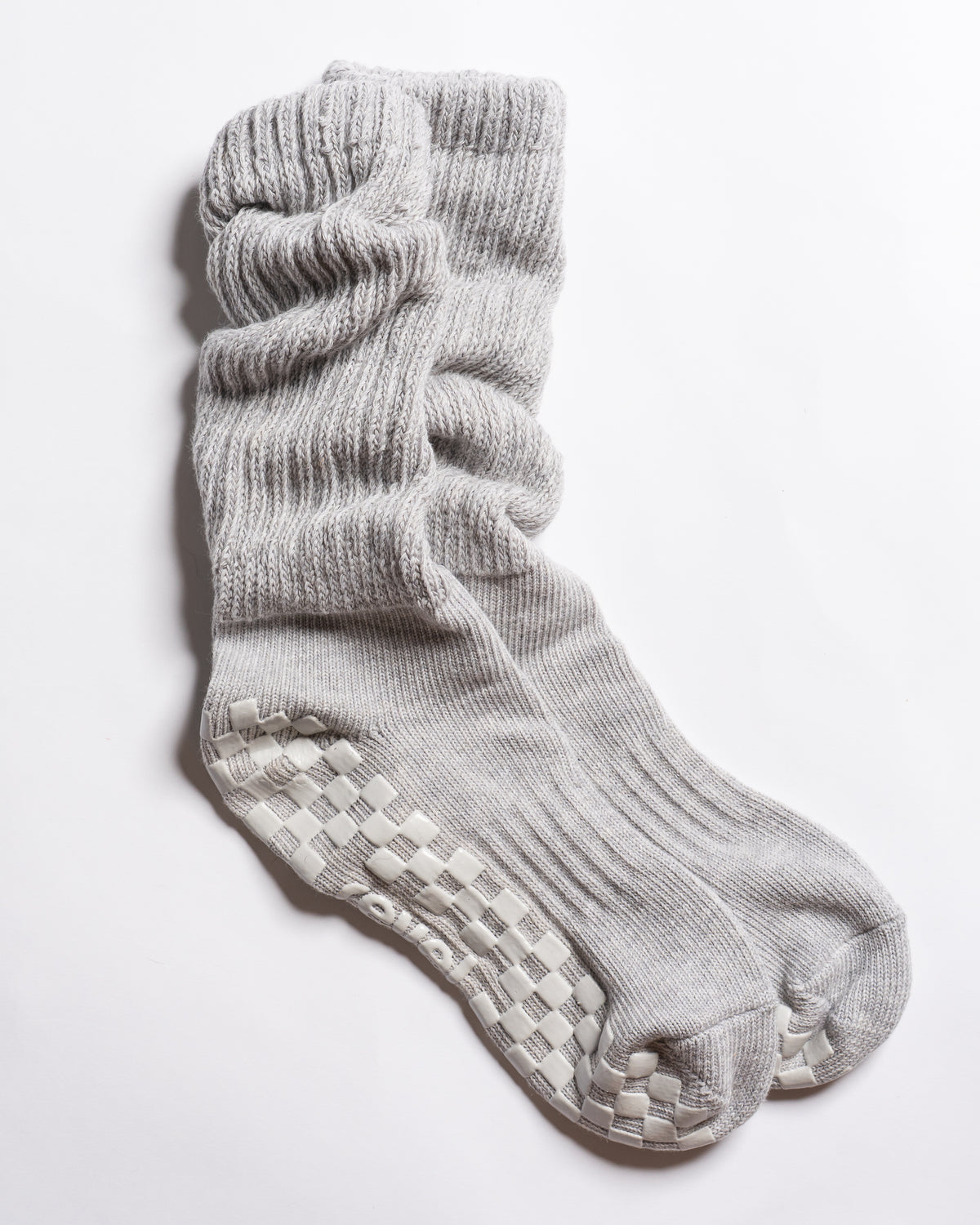 A pair of “The Slouch - Grey” ribbed Pilates grip socks by Revel Athletic, featuring light gray color and textured non-slip grips on the soles, displayed on a white background.