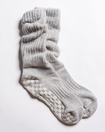 A pair of “The Slouch - Grey” ribbed Pilates grip socks by Revel Athletic, featuring light gray color and textured non-slip grips on the soles, displayed on a white background.