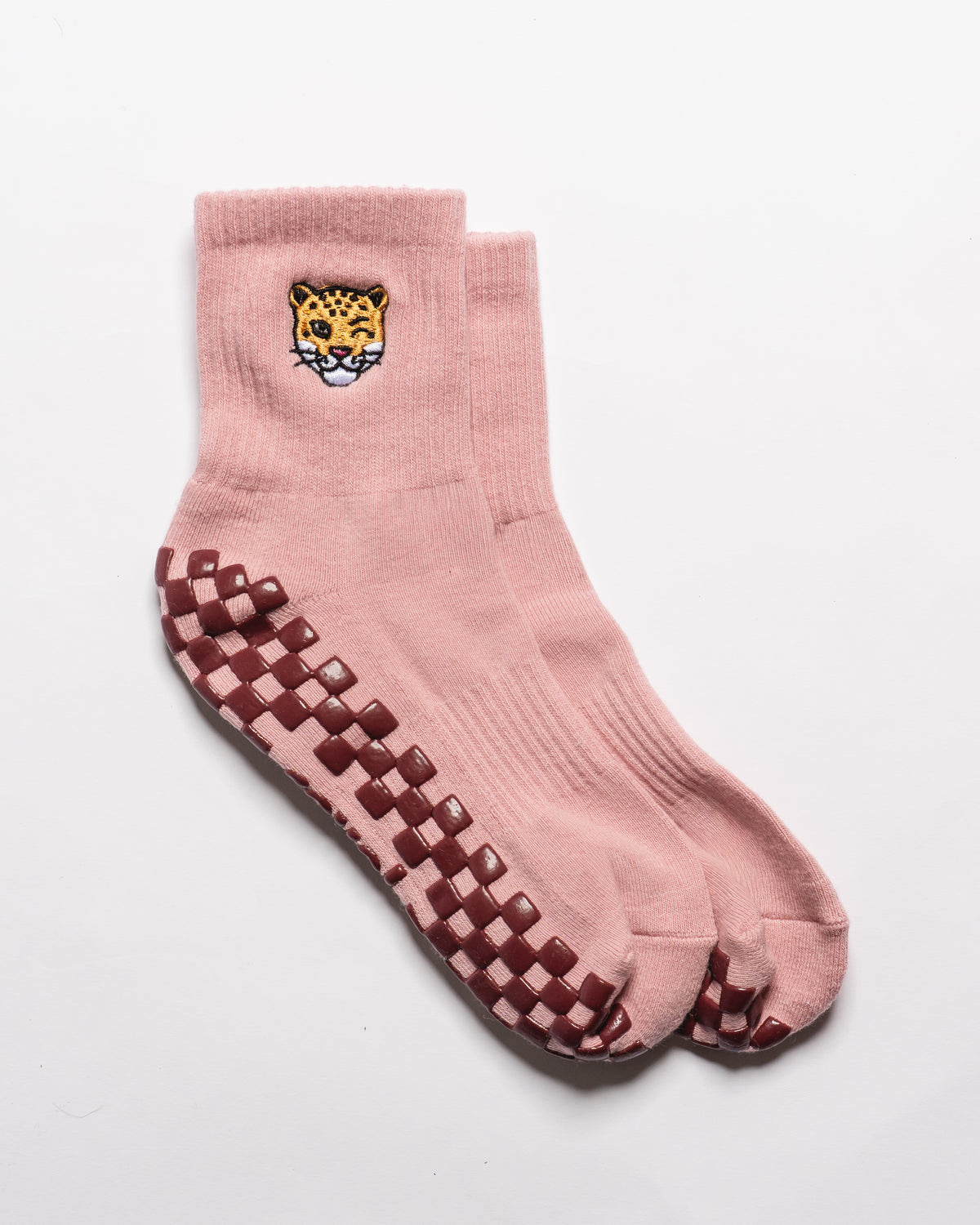 The Wildcat Grip Sock by Revel Athletic features a pink design with leopard embroidery near the top and brown-and-white non-slip grip squares on the soles, displayed on a plain white background—perfect for pilates or everyday comfort.