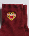 The Sweetheart by Revel Athletic are maroon ribbed crew socks featuring a small heart-shaped patch with a red, blue, yellow, and white plaid embroidery near the top—perfect for Pilates or studio workouts.