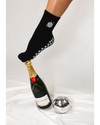A foot in The All Nighter Grip Sock by Revel Athletic—featuring a black sock with a disco ball design—balances on a capped Moët & Chandon champagne bottle, with a small disco ball nearby on a white fabric background, making it the perfect accessory to elevate your Pilates or yoga style.
